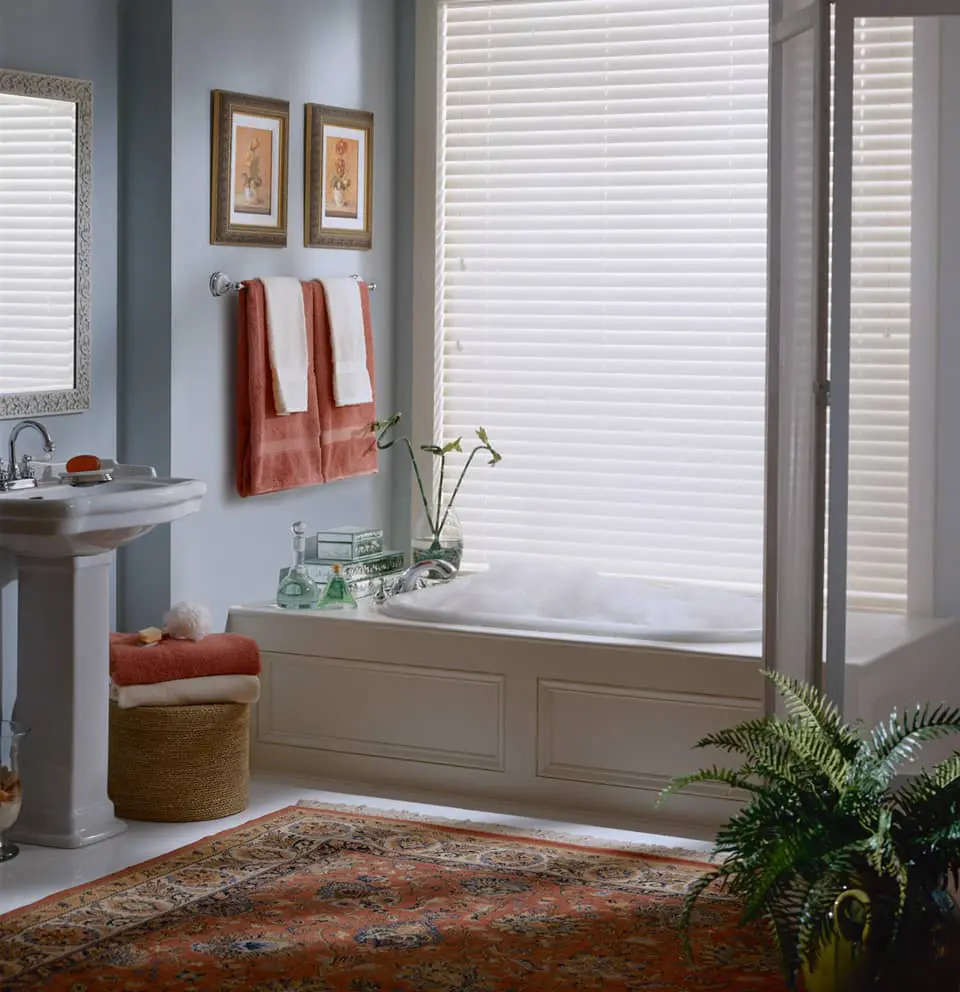 bathroom tub under large window with aluminum blinds