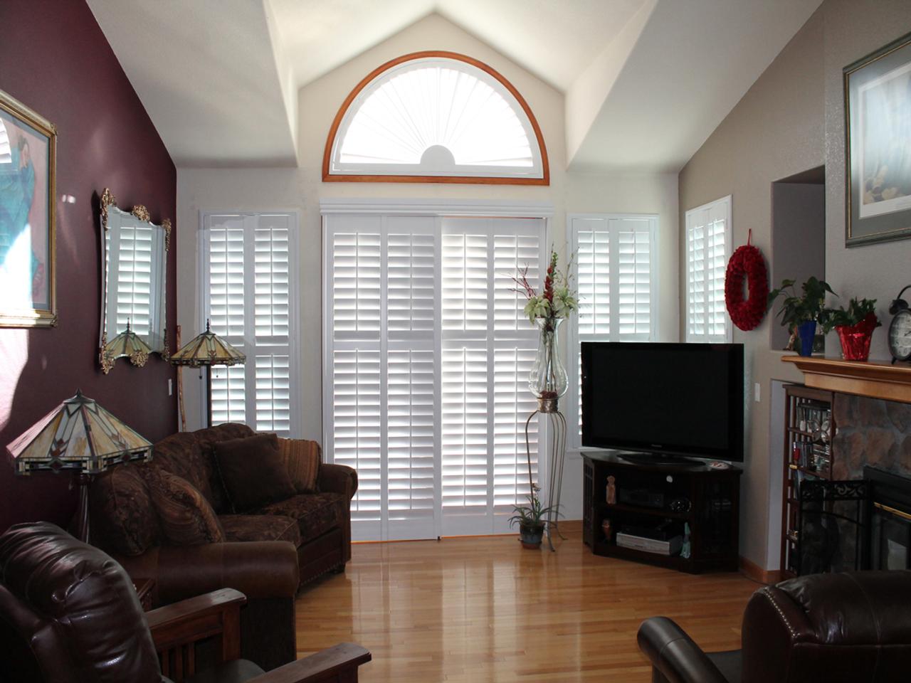 Sliding glass doors with arch over them. Doors and arched window covered with plantation shutters