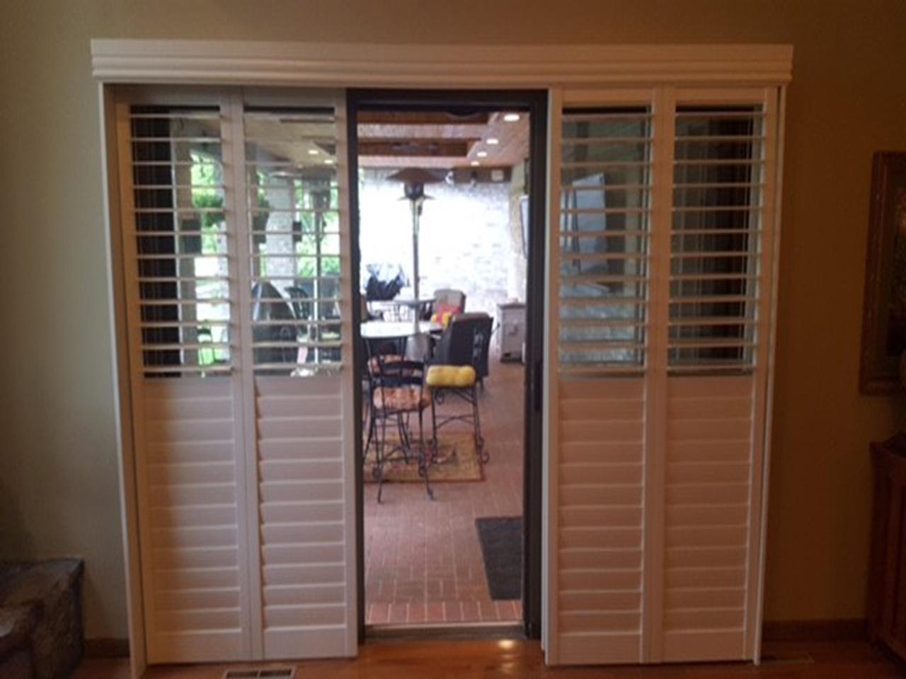 Bypass style plantation shutters pulled to the sides to show the sliding glass door, bottom portion of the louvers in closed position, top louvers open