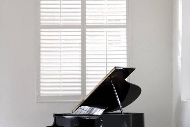 white plantation shutters behind a piano