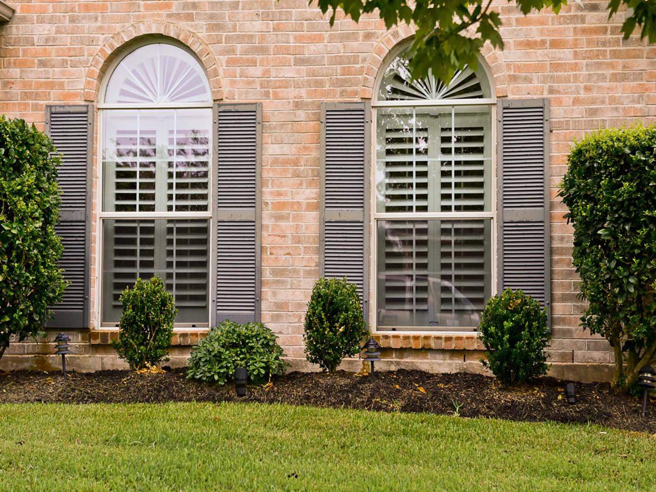 Exterior view of home with arched windows with rectangular shutters and sunburst style shutters on the top