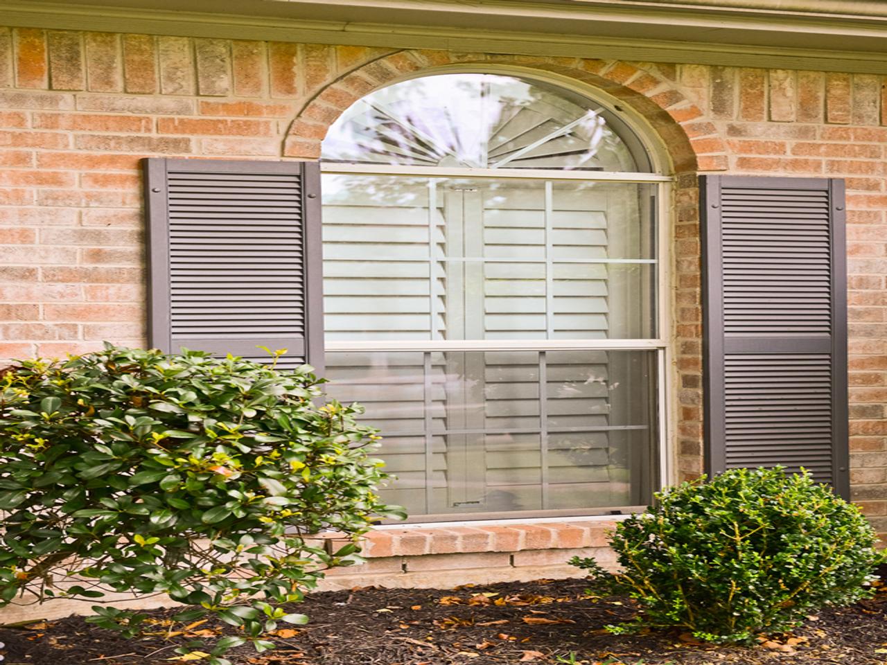 Exterior view of plantation shutters and louvered shutters on a brick house